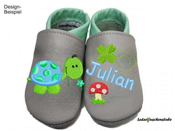 Lederpuschen grau-mint mit rechts Stickerei Schild Blume (mint-hellblau-hellgrün-schwarz) Blume (mint-hellblau) und links Namen (hellblau), Kleeblatt (hellgrün) und Pilz schlicht (rot-weiß-creme-hellgrün)